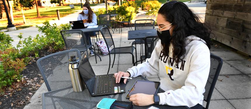 Rowan students with masks on laptops outside. 