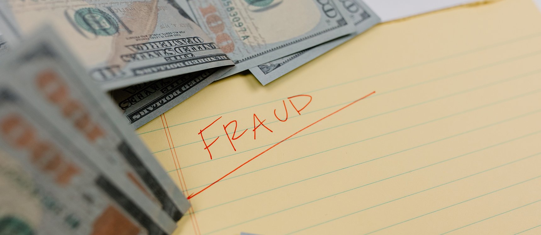 image of a notebook with the word fraud written it surrounded by cash